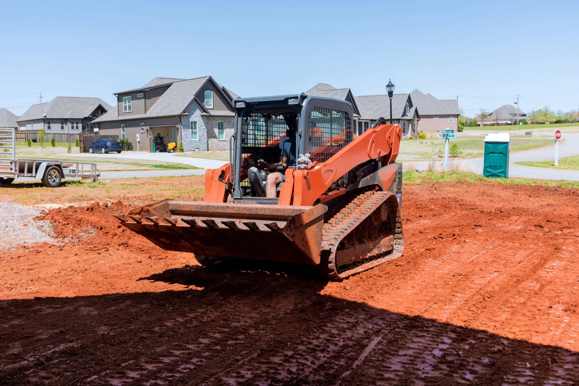 Tracked skid steer grading red dirt on a new home site